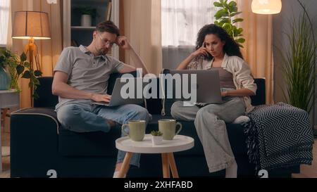 Multiracial couple gadgets addict family computers technology addicted Caucasian man guy male using laptop Hispanic woman girl female typing pc Stock Photo
