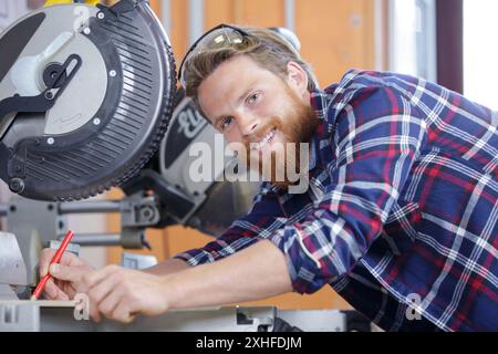 happy workman cutting wooden planks using circular saw in workshop Stock Photo