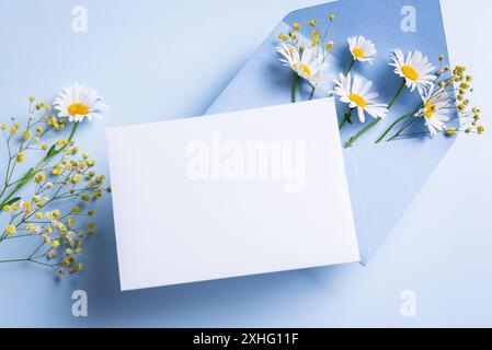 Greeting or invitation card mockup,  white empty blank with envelope and floral decor on bue pastel background, copy space. Creative mockup with white Stock Photo
