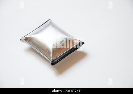 A telephone battery that is swollen from overheating lies on a white background, the phone battery is inflated Stock Photo