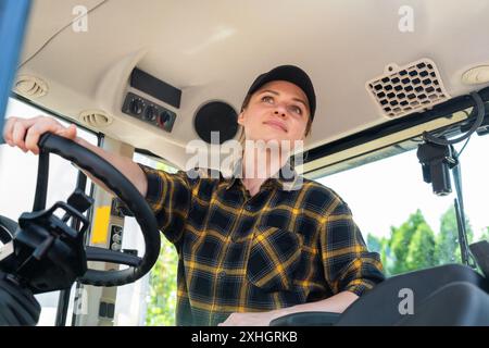 caucasian woman wearing plaid shirt and cap driving construction machinery Stock Photo