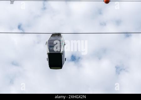 A small car is suspended in the air above a cloudy sky. The car is attached to a cable and he is a ride or a vehicle. The sky is filled with clouds Stock Photo