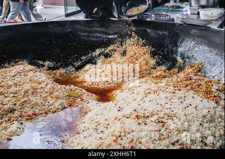 male puts cooked Uzbek pilaf from a large cauldron on a plate in the kitchen. Traditional Oriental Arabic rice cuisine Stock Photo