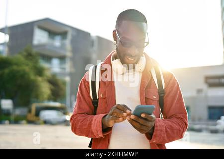 Young happy African Black man standing on city street using mobile phone. Stock Photo