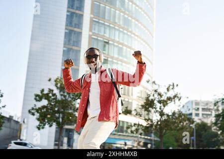 Happy excited young African man in headphones dancing on city street. Stock Photo
