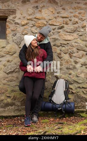 couple of young mountaineers hugging leaning on a shelter wall in the forest Stock Photo
