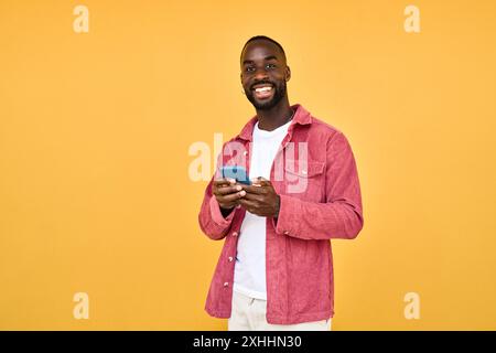 Young happy African man standing isolated on yellow background holding phone. Stock Photo