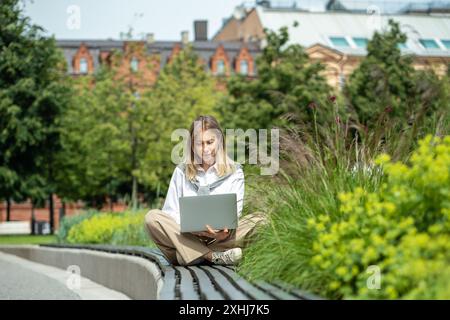 Young business woman remote working on laptop in park, enjoys outdoor workspace as freelancer Stock Photo