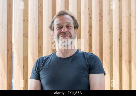 A man with a 50-55 year old beard smiles at the camera as he stands in front of a wooden wall. Stock Photo