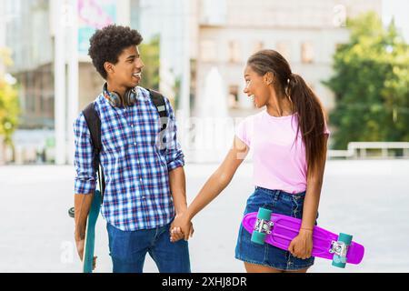 Teen Couple Holding Hands While Walking With Skateboards in City Stock Photo