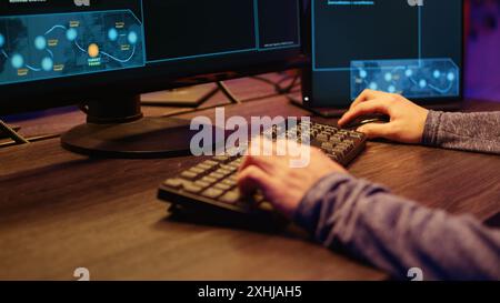 Hacker in secret underground shelter typing on keyboard, writing lines of code on computer, trying to get past security systems with virus. Scammer working on hacking script, close up shot Stock Photo