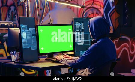 Hackers using green screen PC to code malware designed to exploit network backdoors. Cybercriminals use mockup monitor while bypassing security measures in graffiti painted bunker Stock Photo