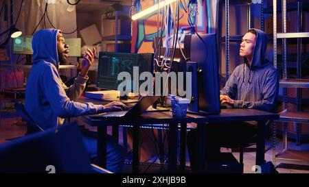 Hackers brainstorming ways to go undetectable by antivirus software installed on systems and successfully trick firewalls, discussing methods of developing zero day exploit in secret bunker Stock Photo