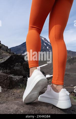 Rear view of female legs in orange skintight running leggings and sneakers. Close-up of lower part of woman's body taken from behind during outdoor fi Stock Photo