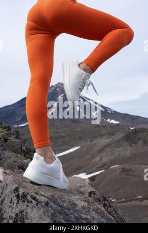 Close-up of fit woman's legs in orange workout leggings and sneakers doing outdoor fitness. Unrecognizable athlete practicing fitness in mountains and Stock Photo