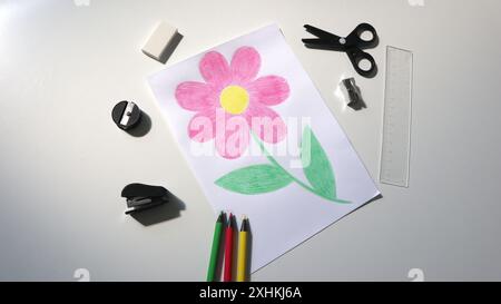 Photo of a child's drawing with colored pencils. Around the picture are colored pencils, scissors, a ruler, an eraser, a sharpener, a stapler. White b Stock Photo