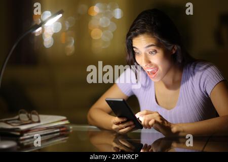 Amazed woman checking phone content in the night at home Stock Photo