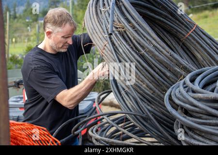 Man working with large coils of black tubing outdoors Stock Photo