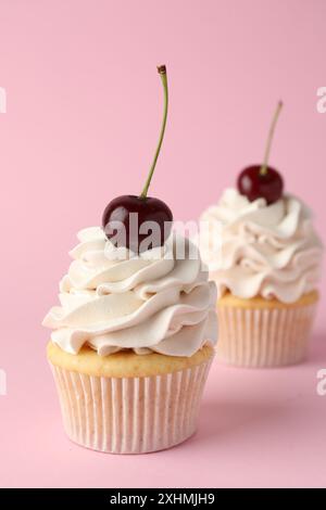 Delicious cupcakes with cream and cherries on pink background Stock Photo