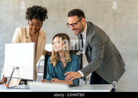 Group of happy multiethnic business people in formal wear gathered around computer in office Stock Photo