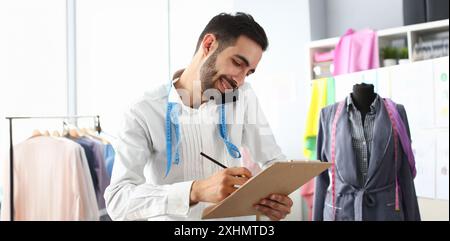 Smiling man tailor speaking on smartphone with client. Designer taking new order in atelier. Sewing workshop or creating new brand concept Stock Photo