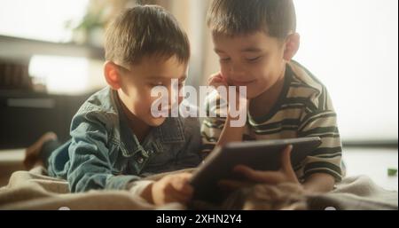 Portrait of Two Male Asian Kids Using a Digital Tablet During Weekend in their Room. Two Cute Siblings Watching Educational Content Online, Sharing the Gadget, and Enjoying their Time Stock Photo