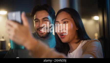 Portrait of a Happy Couple Having Video Call on a Smartphone in a Kitchen at Night. They are Talking and Chatting. Man and Woman Staying Connected to Family and Friends Using Technology and Internet. Stock Photo