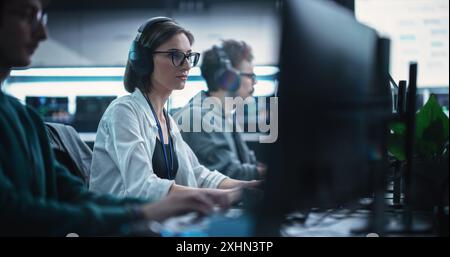 Focused Young Female Software Developer Working on Computer Together with Two Creative Male Colleagues. Data Protection Center with Servers, Storage Hardware and eBusiness Research Stock Photo