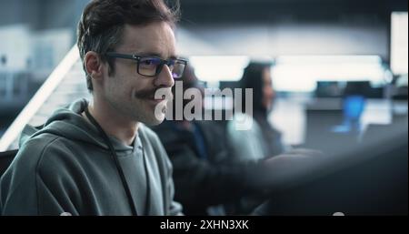Portrait of a Happy Mustachioed Computer Science Team Member Working on a Computer in a Research and Development Technological Center Facility. Smiling Man Writing Code for Industrial Software Stock Photo