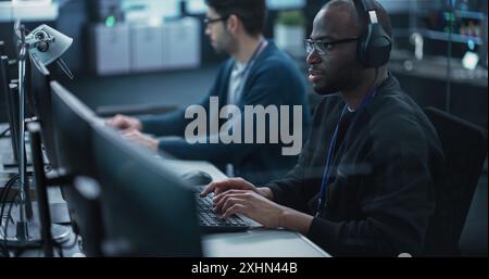 African American QA Engineer Finds and Fixes Bugs in a Product or Program Before the Launch, Collaborating and Talking with Colleague. Young Black Specialist Working in Advanced Technology Industry Stock Photo