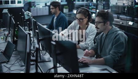 Young Team of Specialists Working on Desktop Computers and Having a Conversation at a Workplace. Female and Male Software Developers Discussing a Solution for Their Artificial Intelligence Project Stock Photo