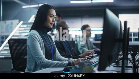 Young Asian Female Software Developer Working on Computer Together with Diverse Creative Colleagues. Data Protection Center with Servers, Storage Hardware and Cyber Security Research Stock Photo
