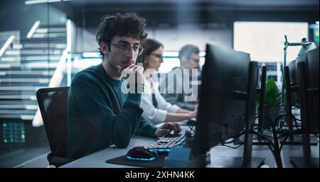 Young Handsome Software Developer Working on Computer in a Technological Laboratory Environment. IT Programming Department Tirelessly Researching and Developing Advanced Commercial Internet Products Stock Photo