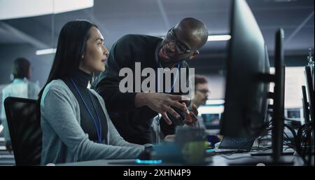 Two Diverse Multiethnic Colleagues Having a Conversation While Busy Working on a Team Project. Asian Female Designer Talking with an African Project Manager. Teamwork in Technology Laboratory Stock Photo