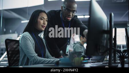 Two Diverse Multiethnic Colleagues Having a Conversation While Busy Working on a Team Project. Asian Female Designer Talking with an African Project Manager. Teamwork in Technology Laboratory Stock Photo