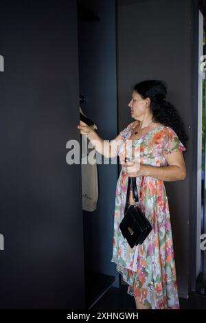 60s businesswoman in floral dress in modern office coworking workspace puts clothes in closet Stock Photo