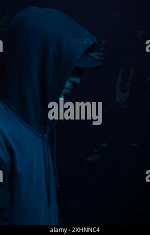 Young man wearing gray sweatshirt hiding his face. Studio portrait. Isolated on blue background. Stock Photo