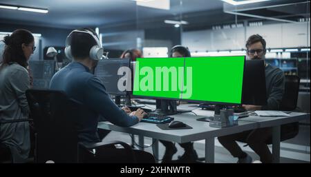 Group of Diverse Multicultural Men and Women Working on Desktop Computers in a Research Center. Young Software Developer Working on a Computer with Two Green Screen Mock Up Displays Stock Photo