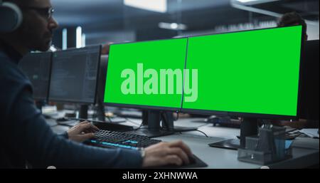 Close Up of a Software Developer Working on a Desktop Computer with Green Screen Mock Up Display. Specialist Typing on Keyboard, Coding and Implementing a New Technical Feature, Working in an Agency Stock Photo