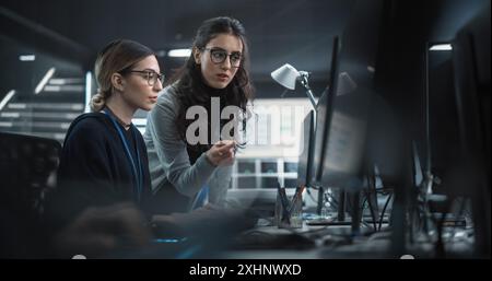 Young Multiethnic Female Software Developer Working on Computer, Discussing Project with Team Leader. Data Protection Center with Servers, Storage Hardware and Cyber Security Research Stock Photo