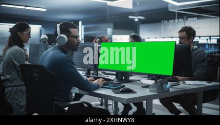 Group of Diverse Multicultural Men and Women Working on Desktop Computers in a Research Center. Young Software Developer Working on a Computer with Two Green Screen Mock Up Displays Stock Photo