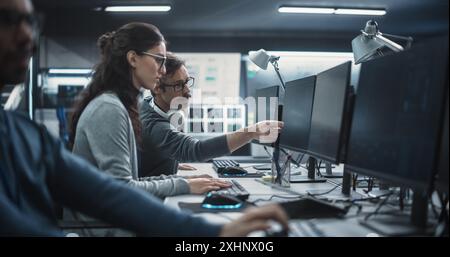 Young Colleagues Working on Computers and Talking at a Workplace. Female and Male Software Developers Discussing a Solution for Their Collaborative Artificial Intelligence Project Stock Photo
