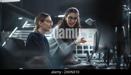 Two Diverse Colleagues Having a Conversation While Busy Working on a Team Project. Multiethnic Female Designer Talking with a Project Manager. Teamwork in Technology Laboratory Stock Photo