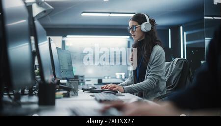 Portrait of a Thoughtful Young Engineer Working on Computer in a Technological Office Environment. Beautiful Multiethnic Woman Wearing Headphones, Writing Software Code for a Blockchain Project Stock Photo