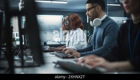 Focused Young African American Female Software Developer Working on Computer Together with Two Creative Male Colleagues. Data Protection Center with Servers, Storage Hardware and eBusiness Research Stock Photo