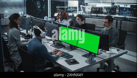 Group of Diverse Multicultural Men and Women Working on Desktop Computers in a Research Center. Young Software Developer Working on a Computer with Two Green Screen Mock Up Displays Stock Photo