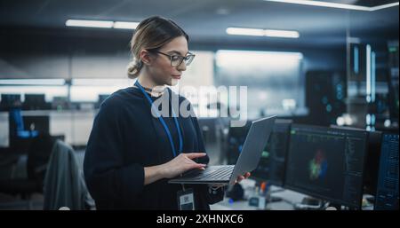Portrait of a Multiethnic QA Engineer Working on Finding and Fixing Bugs in a Product or Software Before the Launch. Female Using Laptop in a Room with Big Green Screen Mock Up Display Stock Photo