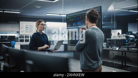 Two Diverse Software Developers Having a Meeting in a Conference Room. Female and Male Tech Industry Engineers Brainstorming Ideas for Their Neural Network Blockchain Startup Stock Photo