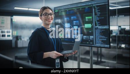 Portrait of a Beautiful Diverse Female Wearing Glasses, Using Laptop Computer, Looking at Camera and Smiling. Information Technology Specialist, Software Engineer or Developer Stock Photo