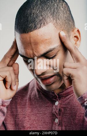 Man in a maroon shirt, pressing his fingers to his temples with a grimace. His expression indicates he is suffering from a headache or significant men Stock Photo